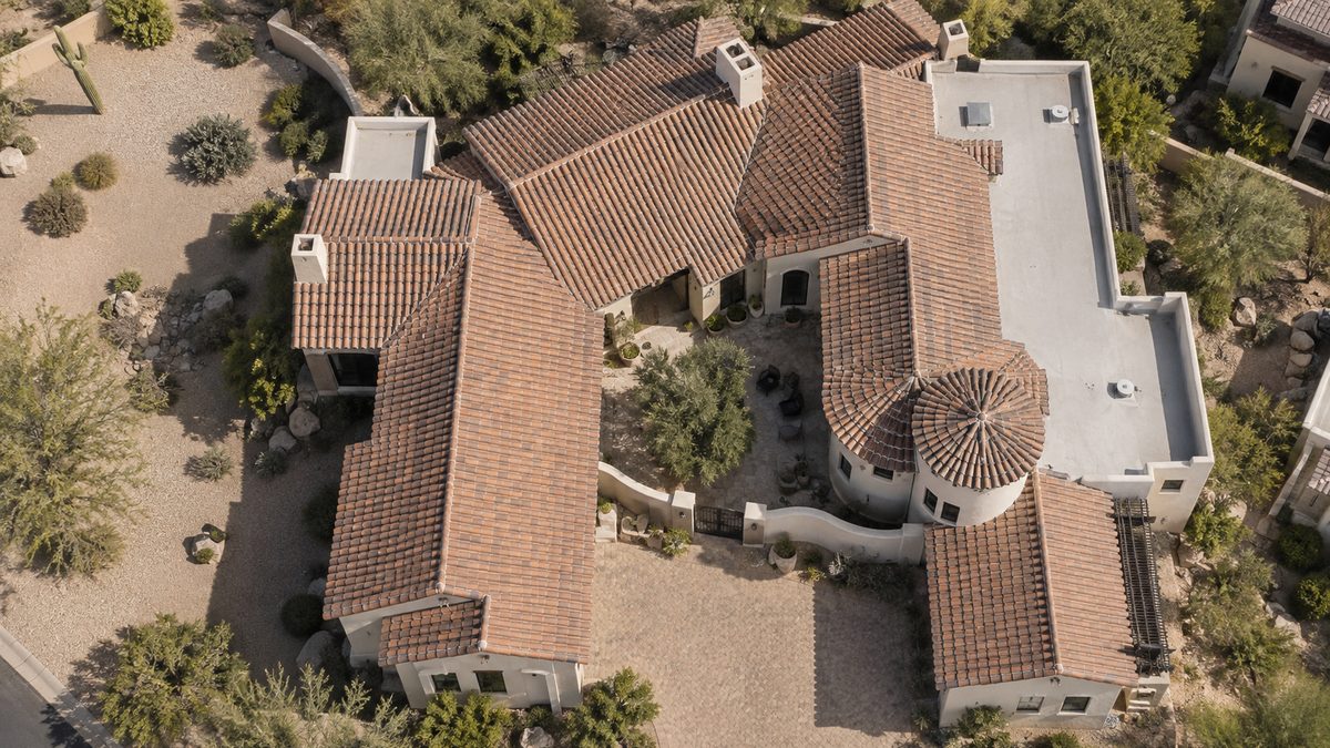 Elevated aerial view of a custom Arizona stucco home with varied tile and flat roof planes and a desert courtyard.